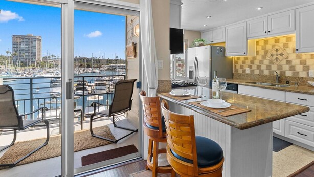 A modern kitchen with a large island, white cabinetry, and a view of a marina. - 302B Amazing Location! Gorgeous Marina Views! Steps from Top Rated Harbor Beach (Oceanside)