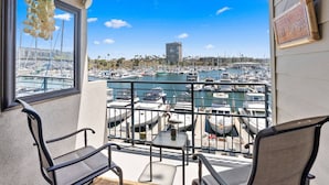 A balcony with two chairs and a small table, overlooking a marina with numerous boats and a tall building in the background. - 302B Amazing Location! Gorgeous Marina Views! Steps from Top Rated Harbor Beach (Oceanside)