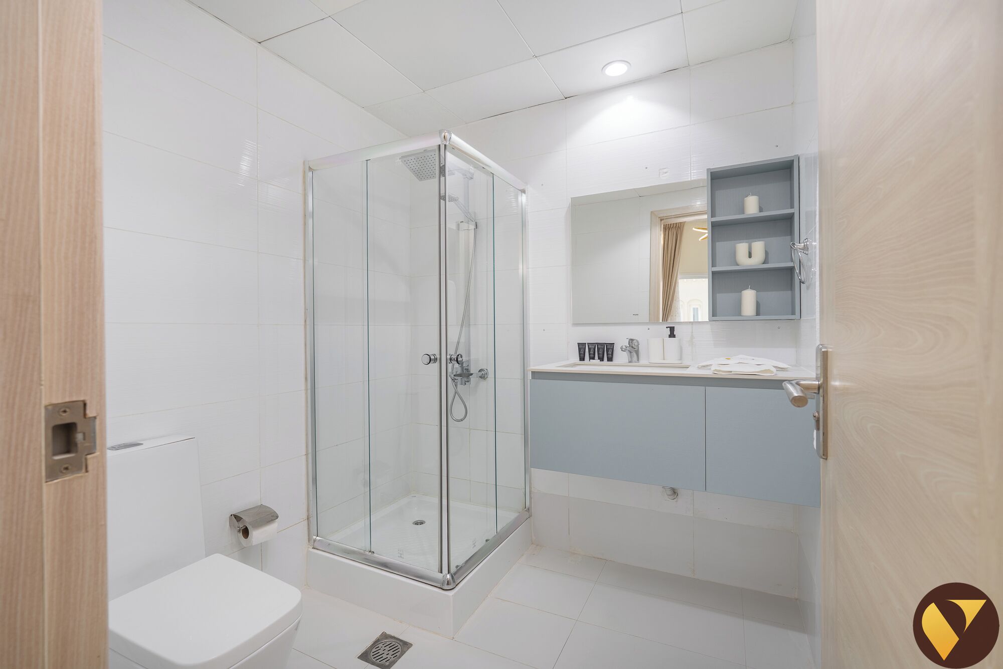 Een moderne badkamer met een douchecabine van glas, een toilet en een wastafel met spiegel en planken.