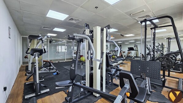 Un gimnasio con diferentes máquinas de ejercicio, espejos y piso de madera.