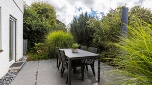 Un patio con una mesa y sillas, rodeado de follaje y un edificio.