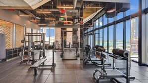 A modern gym with various weightlifting equipment, large windows, and a high ceiling. - Miami Lux Studio 45th floor City and Bay Views (Miami)