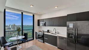 A modern kitchen with dark cabinets, stainless steel appliances, and a large window offering a city view. - Miami Lux Studio 45th floor City and Bay Views (Miami)