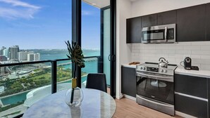 A modern kitchen with a large window, a view of a city and water, and a dining area with a table and chairs. - Miami Lux Studio 45th floor City and Bay Views (Miami)