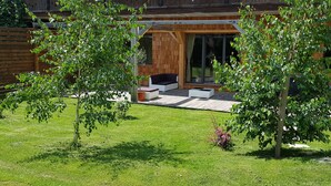 A modern wooden house with a patio area, outdoor seating, and a well-maintained lawn.