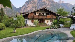 A mountain lodge with a pool, surrounded by lush greenery and mountains.