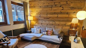 A cozy room with a bed, a chair, a round rug, and wooden walls.
