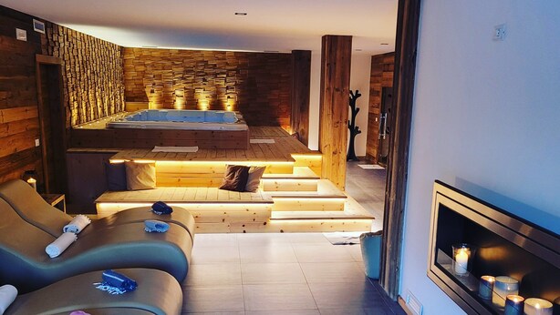 A modern spa room with a massage area, a seating area with a fireplace, and a stone wall.