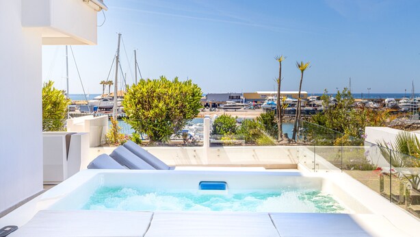 A rooftop pool with a jacuzzi, surrounded by a clear view of the marina and boats.