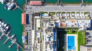 An aerial view of a marina with boats docked, a swimming pool, and a building with balconies.