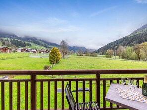 Un balcon avec une balustrade en bois, une table avec une bouteille de champagne et une chaise.