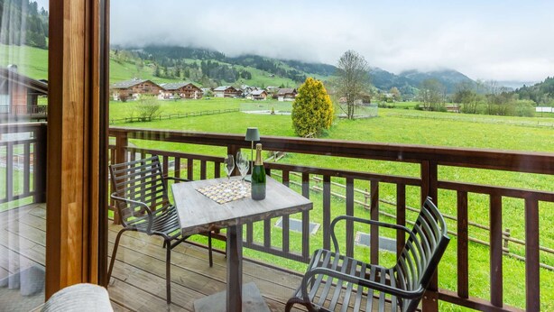 A wooden deck with a table and chairs, overlooking a green valley with houses and mountains. - APARTMENT  LA  CHAPELLE D'ABONDANCE - Oasis B107 (LA CHAPELLE D ABONDANCE)