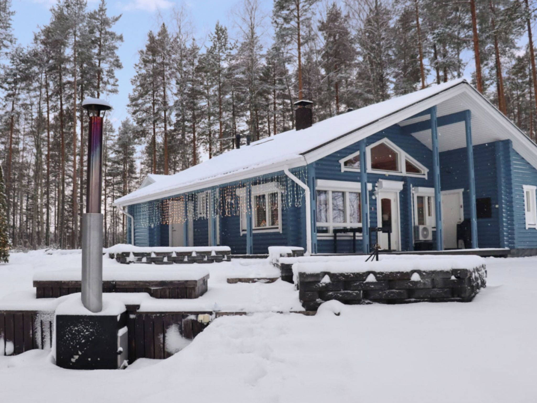 A snow-covered cabin with a porch, surrounded by a forest.