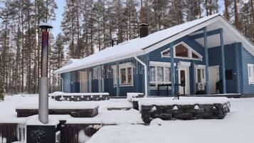 A snow-covered cabin with a porch, surrounded by a forest.