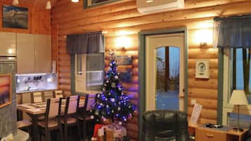 Ein gemütliches Blockhaus-Interieur mit Essbereich, einem Weihnachtsbaum, einem Ledersessel und einem kleinen Tisch.