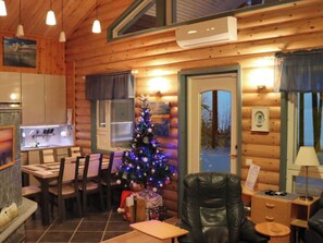 L’intérieur d’un chalet accueillant, avec un coin repas, un sapin de Noël, un fauteuil en cuir et une petite table.