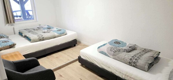 Una habitación pequeña y limpia con dos camas, una silla y una ventana con vistas.