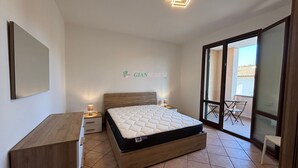 A bedroom with a bed, bedside tables, a wooden dresser, a sliding glass door leading to a balcony, and a wall-mounted light fixture. - 5 beds with private parking space Ref. Costanza (San Vincenzo)