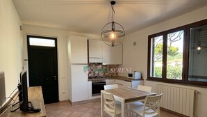 A compact kitchen with white cabinets, a wooden table, and chairs. There is a window with a view of greenery outside. - 5 beds with private parking space Ref. Costanza (San Vincenzo)