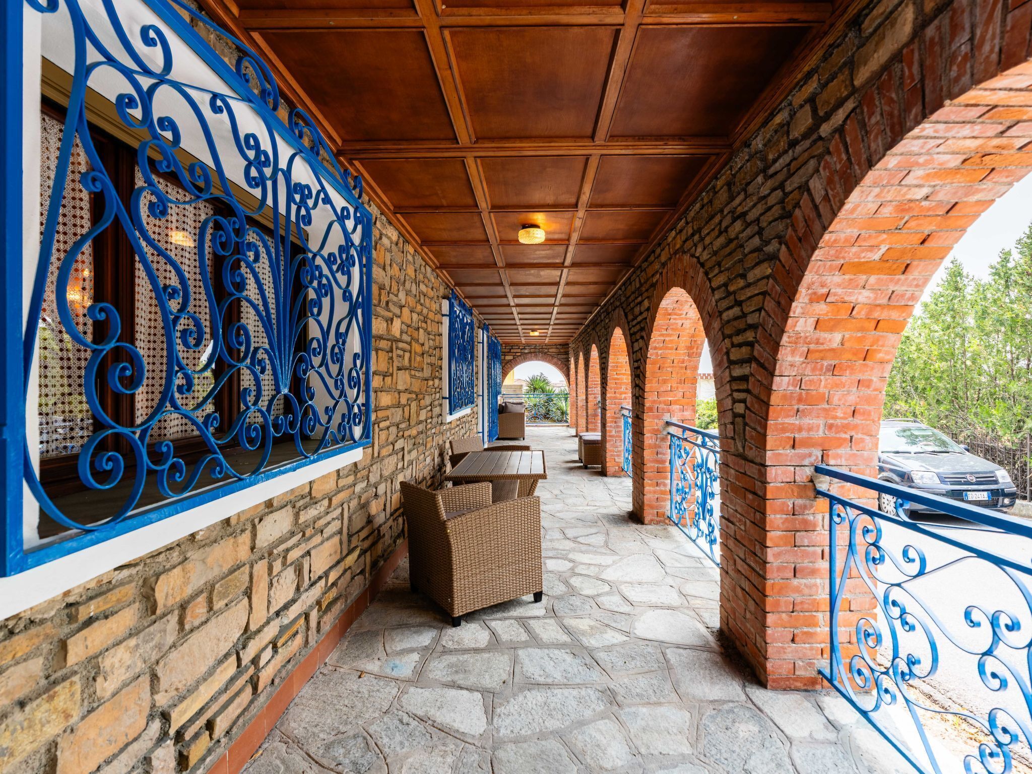 A covered outdoor area with brick walls, blue metal railings, and stone flooring.
