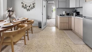 Eine moderne Küche mit Holzausbau, ein Essbereich mit Tisch für vier Personen und ein Gang, der in ein weiteres Zimmer führt.