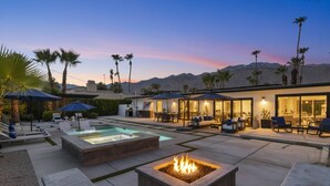 A modern outdoor patio with a pool, fire pit, and seating areas, surrounded by palm trees and mountains in the background. - Private Pool and Spa in Palm Springs with Mountain Views and Designer Interiors (Palm Springs)
