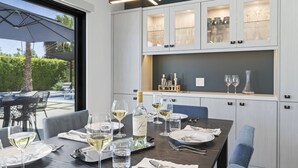 A dining area with a table set for four, featuring wine glasses, plates, and a bottle of white wine. There are chairs around the table, and a view of the outdoors through a large window. - Private Pool and Spa in Palm Springs with Mountain Views and Designer Interiors (Palm Springs)