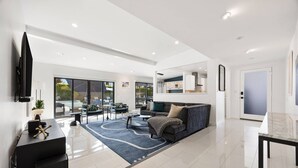 A modern living room with a sofa, coffee table, and TV. There is a dining area with chairs and a table. The room has large windows and a view of the outdoors. - Private Pool and Spa in Palm Springs with Mountain Views and Designer Interiors (Palm Springs)