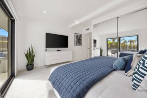 A modern bedroom with a large bed, a flat-screen TV, a white dresser, and a sliding glass door leading to a balcony. - Private Pool and Spa in Palm Springs with Mountain Views and Designer Interiors (Palm Springs)