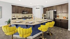 Une cuisine moderne avec des meubles de couleur bois foncé, des plans de travail en granit, un îlot central doté de tabourets de bar et un réfrigérateur.