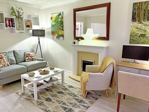 Uma sala de estar com sofá, poltrona, mesa de centro, lareira, televisão e estantes de livros.