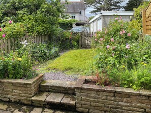 A stone wall with steps leading to a grassy area, surrounded by various plants and flowers.