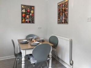 Un comedor con una mesa dispuesta para cuatro personas, sillas, un radiador e imprime botánicas enmarcadas en la pared.