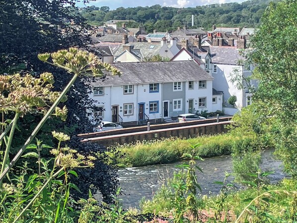 A riverside building with a bridge, surrounded by greenery and a residential area.