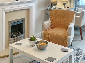 A modern living room with a fireplace, a comfortable armchair, a small table with a bowl of snacks, and a laptop.