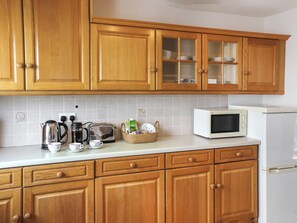 Een keuken met houten kastjes, een magnetron, een waterkoker en een broodrooster.