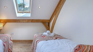 A bedroom with two beds, a skylight, wooden beams, and a view of trees. - Y Llaethdy - UK49916 (Pen-clawdd)