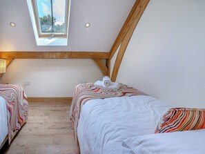 Ein Schlafzimmer mit zwei Betten, einem Oberlicht, Holzbalken und Blick auf Bäume.