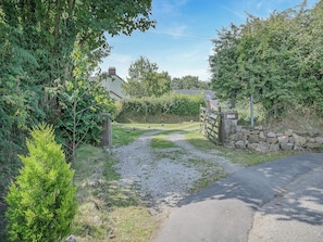 A rural pathway leading to a stone wall and a gated entrance, surrounded by greenery and a house in the background. - Y Llaethdy - UK49916 (Pen-clawdd)