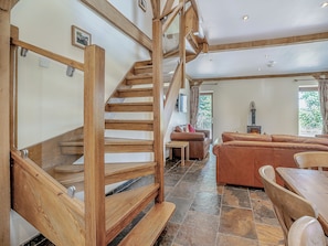 Eine Holztreppe führt zu einem Schlafzimmer auf dem Dachboden, einem Wohnbereich mit Sofa und Kamin sowie einem Esstisch mit Stühlen.