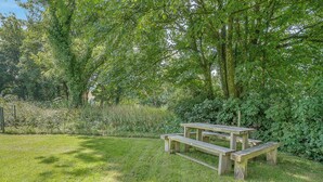 A wooden picnic table in a grassy area with trees and bushes in the background. - Y Llaethdy - UK49916 (Pen-clawdd)