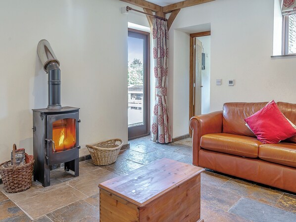 A cozy living room with a wood-burning stove, a leather sofa, and a stone-tiled floor.