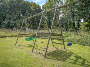 A wooden swing set in a grassy area with trees in the background.