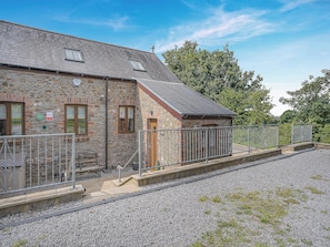 A stone building with a metal fence, a gravel area, and a clear sky. - Y Llaethdy - UK49916 (Pen-clawdd)