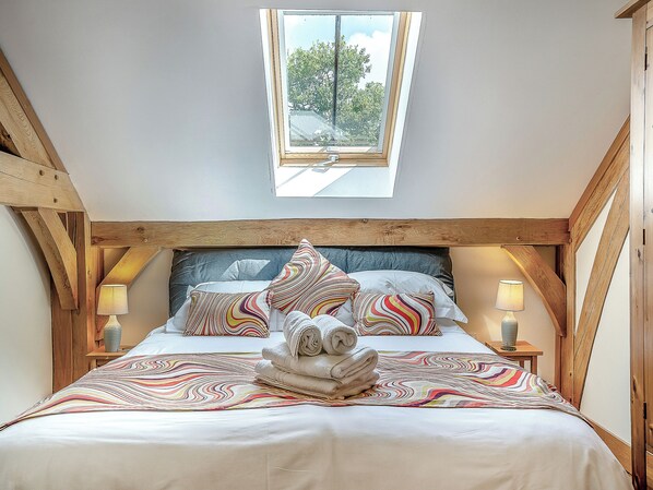 A bedroom with a sloped ceiling, a skylight, a bed with patterned bedding, two bedside lamps, and a stack of towels.
