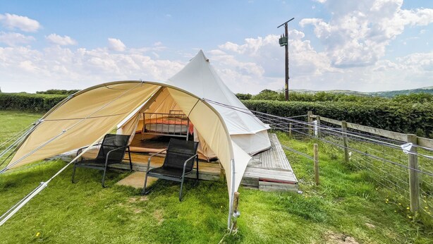 A tent with a bed and two chairs, set up on a grassy field with a wooden fence and a utility pole in the background. - 1 bedroom accommodation in Abergele (Abergele)