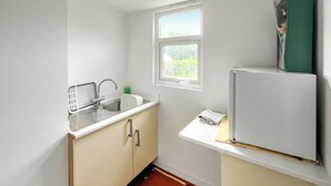 A compact kitchen with a sink, a window, and a refrigerator. - 1 bedroom accommodation in Abergele (Abergele)