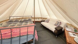 A tent interior with a bed, sofa, and wooden table. - 1 bedroom accommodation in Abergele (Abergele)