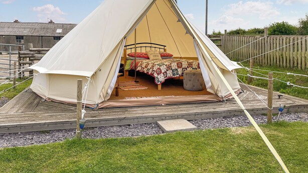 Uma tenda com cama por dentro, rodeada por um deck de madeira e uma área gramada.