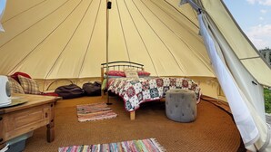 Interior acolhedor de uma tenda com uma cama, uma mesa e um banquinho estofado.